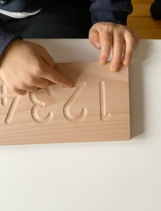 Young child using a Montessori wooden number board to finger trace numbers to help support early writing skills