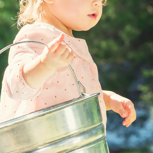 Child independently carries a bucket to complete a gardening task independently