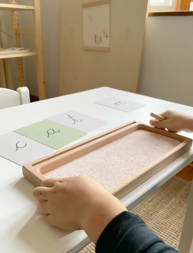 Young child using a Montessori sand writing tray for early writing skills